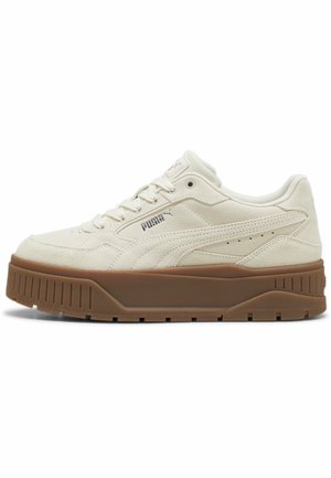 Sneakers basses Puma en daim crème avec semelle épaisse en caoutchouc marron et laçage à l'avant, logo Puma sur le côté sur fond blanc propre.
