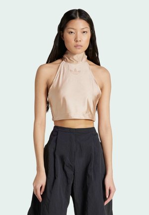 Top corto halter de color beige claro en tejido satén con cuello alto, que cuenta con un logo sutil y costuras laterales. Combinado con pantalones de pierna ancha en color azul marino.