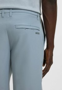 Light blue trousers made of smooth fabric, featuring a back pocket with a curved opening and a printed "BOSS" logo near the right pocket.