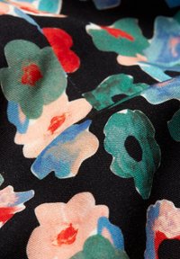 Tissu noir avec un motif floral présentant de grandes fleurs rose clair et bleues, ainsi que de plus petites accents rouges et verts. Texture douce.