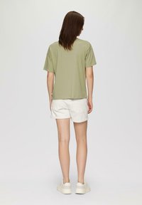 Oliwkowa koszulka z krótkim rękawem w zestawie z białymi szortami. Koszulka ma luźny fason i prosty dół. Obuwie to kremowe trampki.