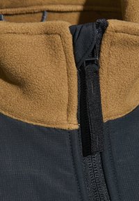 Fleecejacke mit einem strukturierten, braunen Kragen und dunklem Stoff. Verfügt über einen schwarzen Reißverschluss und kontrastierende Stickdetails.