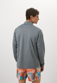 Camisa gris de manga larga con cuello, combinada con pantalones cortos de vivos colores en naranja, azul y blanco, que presentan diseños abstractos.