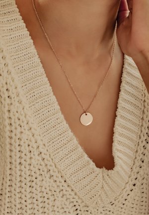 Rosenvergoldete, runde Anhänger-Halskette an feiner Kette, präsentiert vor einem strukturierten cremfarbenen Strickpullover mit weitem Ausschnitt.