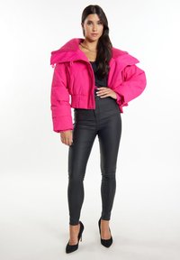 Giacca puffer tagliata fucsia con finitura testurizzata e colletto oversize, abbinata a pantaloni in pelle nera aderenti e tacchi alti neri.