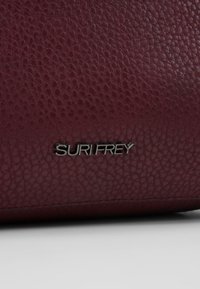 Sac en cuir bordeaux avec surface texturée et marquage argenté "SURI FREY", arborant un design épuré et minimaliste avec des bords cousus.