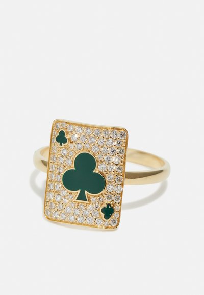 Anillo de oro con un diseño rectangular, que presenta un prominente símbolo de trébol verde rodeado de pequeñas piedras claras como embellishment.