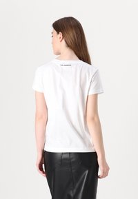 Baltas trumpas rankovėmis T-shirt, pagamintas iš medvilnės, su siūtu apykakle. Nugarinėje pusėje virš apykaklės yra etiketė "KARL LAGERFELD".