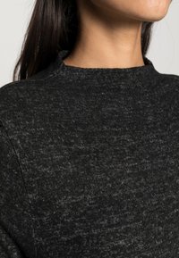Maglione nero con texture e collo alto, realizzato in un morbido tessuto leggermente melangiato e dal taglio casual, mostrato dalla spalla in su.