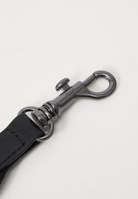 Black leather strap with a shiny black metal clip. Clip features a round latch and engraved branding detail, attached to a loop.