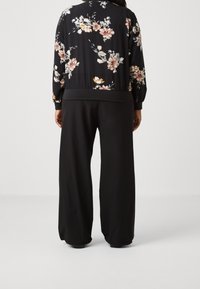 Černá květinová bomber bunda s černým pasem, zdobená barevným květinovým vzorem. Kombinováno s volnými černými kalhotami.