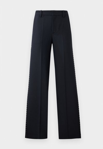 Pantalons larges en noir. Coupe ajustée avec une texture lisse. Présente une rangée de clous métalliques le long des coutures latérales pour le détail.