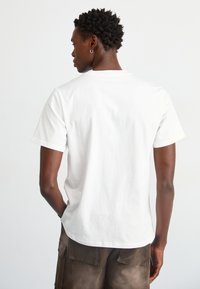 T-shirt bianca in cotone con maniche corte, scollatura rotonda e design semplice. La vista posteriore mostra un tessuto morbido e bordi puliti.