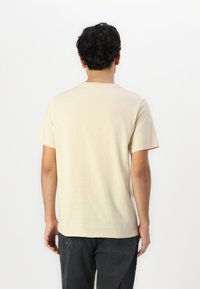 Camiseta beige de manga corta con escote redondo y textura suave, combinada con pantalones de pana oscuros que presentan un sutil patrón acanalado.