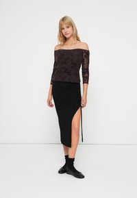 Avskjærmet, gjennomsiktig svart topp med blomstermønster kombinert med et svart, knelengde skjørt med sidespalte og samlet detalj.