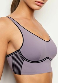 Reggiseno sportivo viola chiaro con dettagli neri, una texture liscia, scollatura a barca e un design a righe sui lati. Spalline regolabili.