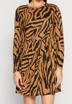 Kobieta ubrana w brązową i czarną sukienkę w paski tygrysa z długim rękawem, dopasowaną w talii i z rozkloszowanym dołem.