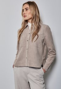 Beige suedine overhemd met knopen, twee borstzakken, een klassieke kraag en een relaxte pasvorm. Soepele textuur met subtiele lijnen.