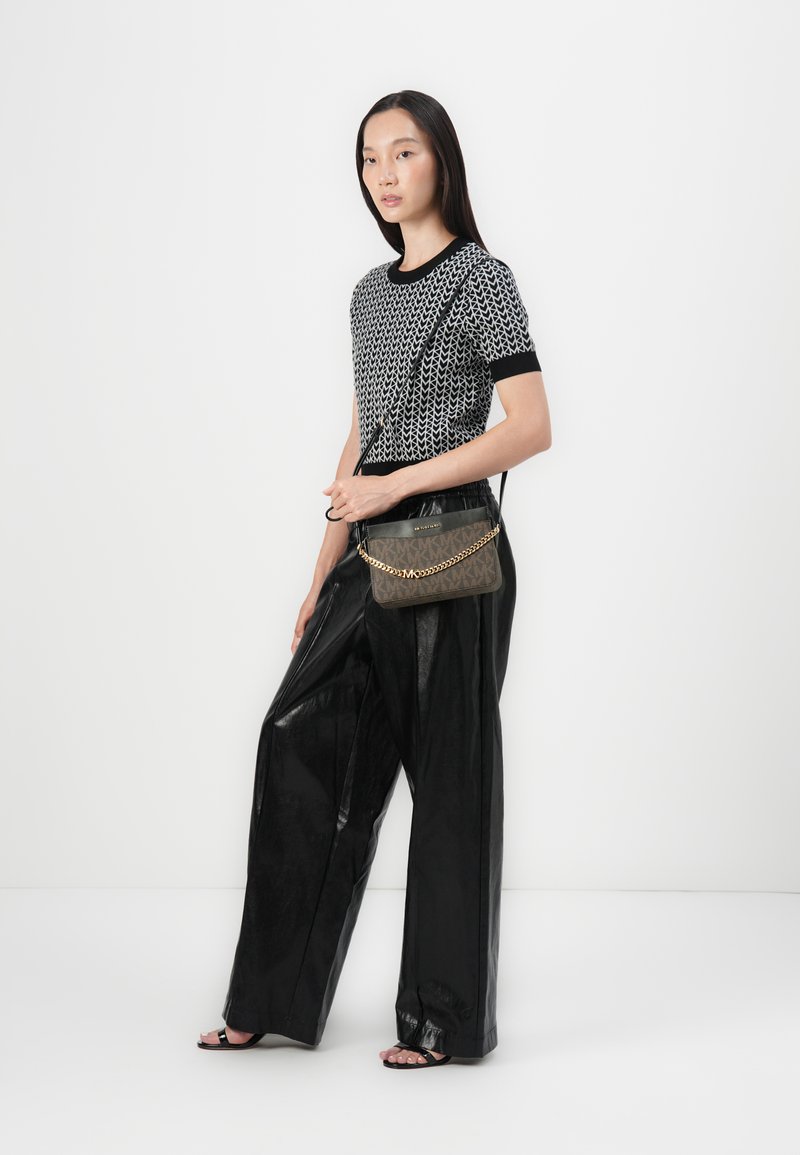 Zwart-wit geblokte top met korte mouwen, gecombineerd met glanzende zwarte wijde broek, en een donkere tas met een gouden schouderband.