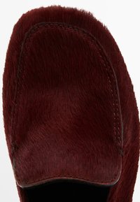 Mocassino in pelliccia sintetica bordeaux con punta arrotondata, dettagli di cucitura in vista e rivestimento interno liscio. Tessuto morbido.