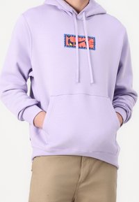 Ljuslila huvtröja med en frontficka, dragsnodd på huvan och en flerfärgad logotyp med blå kant och röd design.