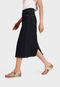 Gonna midi in denim scuro con spacchi laterali, decorata con cuciture dorate e tasche. Abbinata a sandali beige con zeppa, dotati di una fascia e una fibbia.