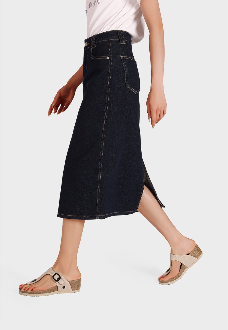 Gonna midi in denim scuro con spacchi laterali, decorata con cuciture dorate e tasche. Abbinata a sandali beige con zeppa, dotati di una fascia e una fibbia.