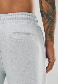 Lichtgrijze sweatpants met een gestructureerd oppervlak. Elastische tailleband en een enkele achterzak, met een eenvoudig, gestikt ontwerp.
