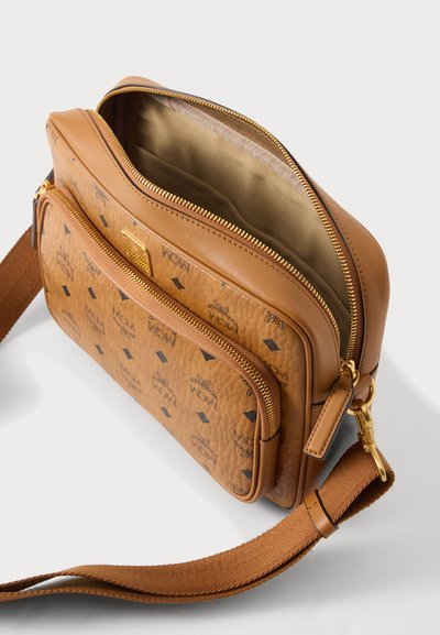 Ταμπά δερμάτινη τσάντα χιαστί με μπροστινή τσέπη με φερμουάρ, ρυθμιζόμενο καφέ υφασμάτινο λουρί, χρυσά μεταλλικά στοιχεία και ανοιχτό κύριο διαμέρισμα που δείχνει μπεζ επένδυση στο εσωτερικό.