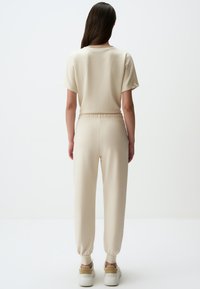 Beige jumpsuit met korte mouwen, elastische tailleband en taps toelopende benen. Gemaakt van zachte stof, met een minimalistisch ontwerp en geen zichtbare patronen.