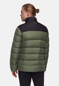 Vadderad jacka med grön kropp och svart övre del. Har en hög krage, horisontell söm och en logotyp på baksidan.