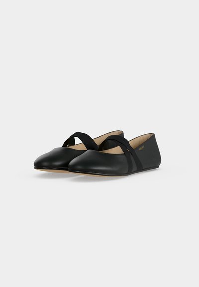 Paire de ballerines en cuir noir avec bouts arrondis et brides élastiques croisées sur fond blanc.