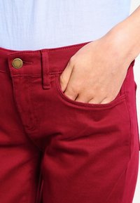 Pantalones de mezclilla rojos con un ajuste slim, que cuentan con un bolsillo frontal y un botón de latón en la cintura. Material de algodón con una textura suave.