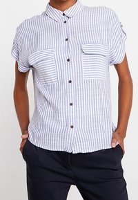 Koszula w jasnoniebiesko-białe paski z krótkimi rękawami, dwoma kieszeniami na piersi i brązowymi guzikami; wykonana z teksturowanej, przewiewnej tkaniny.