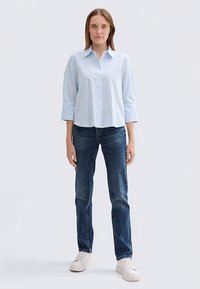 Svetlo modra in bela srajca s pasovi in gumbi, z rokavi dolžine tri četrtine, kombinirana s temno modrimi jeans hlačami in belimi supergami.