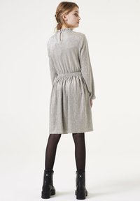 Robe argentée avec une finition texturée et brillante, taille élastique, manches longues et dos en clé. Portée avec des bottines noires et des collants.