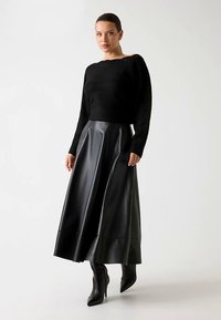 Pull en tricot noir avec un large décolleté, associé à une longue jupe en cuir noir. La jupe a une texture lisse et brillante ainsi qu'une coupe évasée.