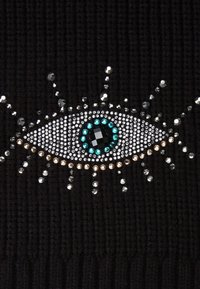 Il tessuto a maglia nero presenta un design di occhio ben in evidenza, decorato con strass argento, turchese e trasparenti, creando un effetto visivo texturizzato.