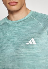 Light blue athletic shirt made of textured fabric with a crew neckline, featuring a white Adidas logo on the chest.