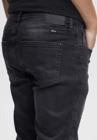Zwarte denim jeans met een slim fit, voorzien van achterzakken en subtiele stikdetails. De tailleband bevat een zwarte leren patchlabel.