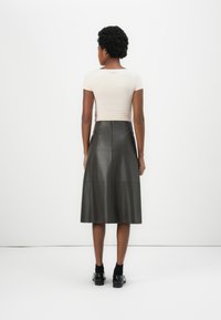 Beige tettskjorte i slim fit kombinert med et mørkegrønt skinnskjørt til kneet. Skjørtet har en glatt tekstur og en skjult glidelås bak.