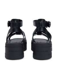 Μαύρα σανδάλια πλατφόρμας με ανοιχτή μύτη, παχύ πέλμα και ρυθμιζόμενα λουράκια στον αστράγαλο. Κατασκευασμένα από λείο, ανθεκτικό υλικό με λεπτομέρεια λογότυπου.