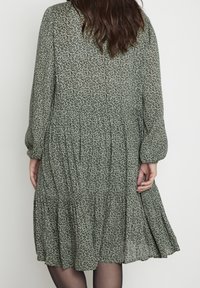 Zielona sukienka w kwiatowy wzór z długimi rękawami, tierowanym dołem i elastycznymi mankietami, uszyta z lekkiego materiału, oferująca swobodny krój.