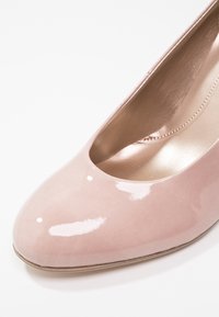 Chaussure pour femme à talon haut, rose clair brillant, avec bout arrondi, coutures visibles le long de la doublure intérieure et texture en cuir lisse.