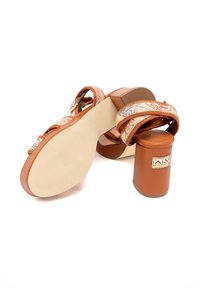 Sandali con tacco color marrone con cinturini decorati, dotati di un tacco a blocco e una suola testurizzata. Accompagnati da un'etichetta di marca sul tacco.