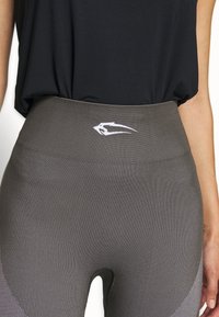 Harmaat korkeavyötäröiset legginsit, joissa on pystysuora ribbikuvio, valkoisella logolla vyötärönauhassa, yhdistettynä löysään mustaan toppiin.