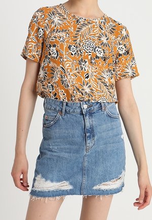 Top corto de flores naranjas con detalles negros, combinado con una falda de mezclilla azul clara con dobladillos deshilachados y detalles rasgados.
