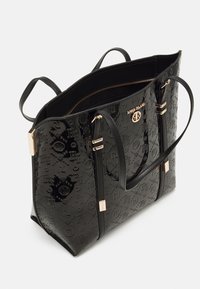 Czarna torebka typu tote z lakierowanej skóry, z wytłoczonym wzorem logo, złotymi okuciami, podwójnymi uchwytami i zamkiem błyskawicznym u góry.