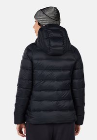 Giacca a vento nera con cappuccio, caratterizzata da un design trapuntato e una texture liscia. Indossata con un berretto a righe bianche e nere.