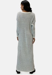 Abito lungo grigio a maglia con coste verticali, caratterizzato da un ampio scollo e maniche lunghe, rifinito con un bordo più chiaro ai lati.